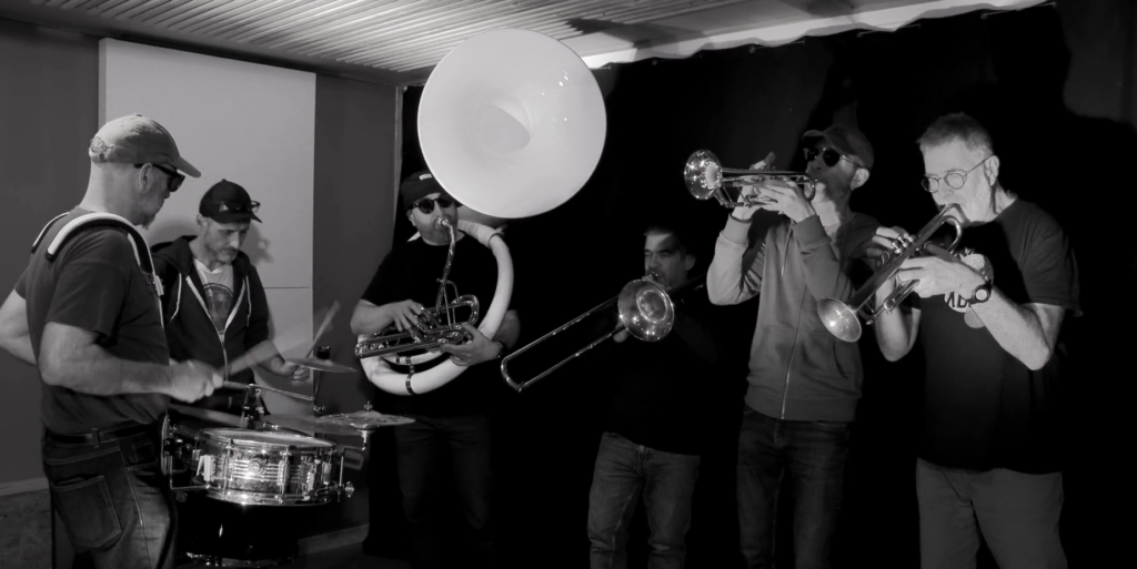photo en noir et blanc du groupe en plein action dans le studio du chêne percé. De gauche à droite, 2 percussionistes, un soubassophone, 1 trombonistes et 2 trompettistes.